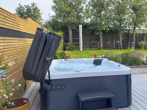 Ein Whirlpool auf einer Holzterrasse mit Holzzaun und Grünpflanzen im Hintergrund.