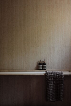 A bathroom with a tiled wall, a towel hanging on the wall, and two bottles on a shelf. - Sa Roca Blanca (S'Horta)
