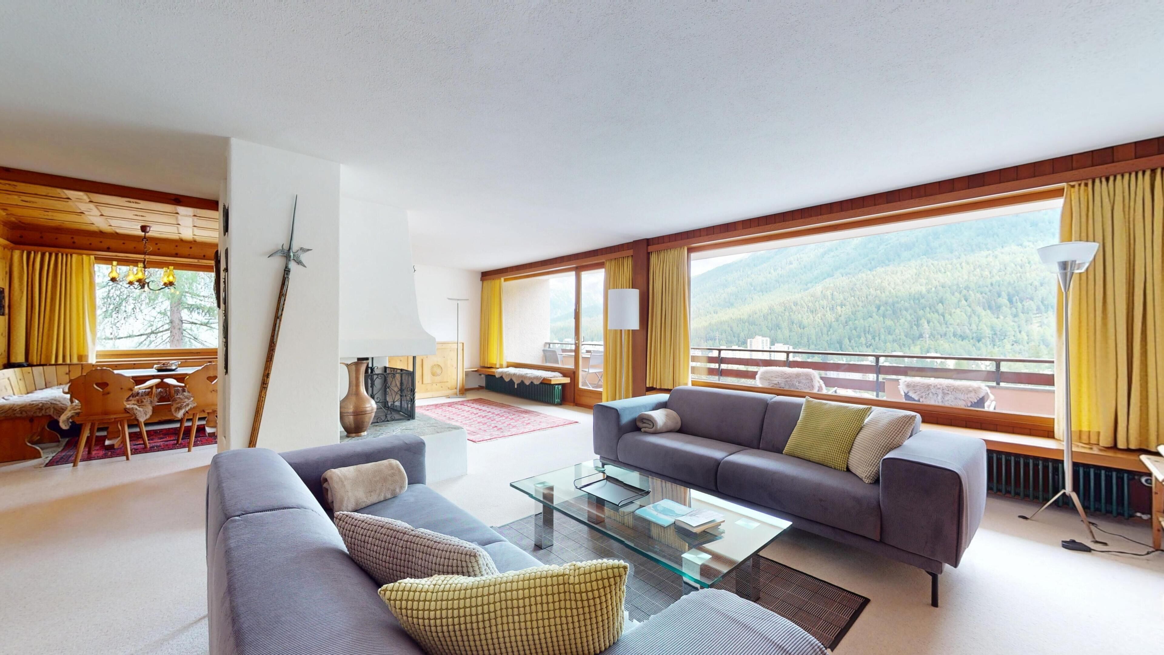 Ein modernes Wohnzimmer mit einer Couch, einem Glastisch und Blick auf eine Berglandschaft.