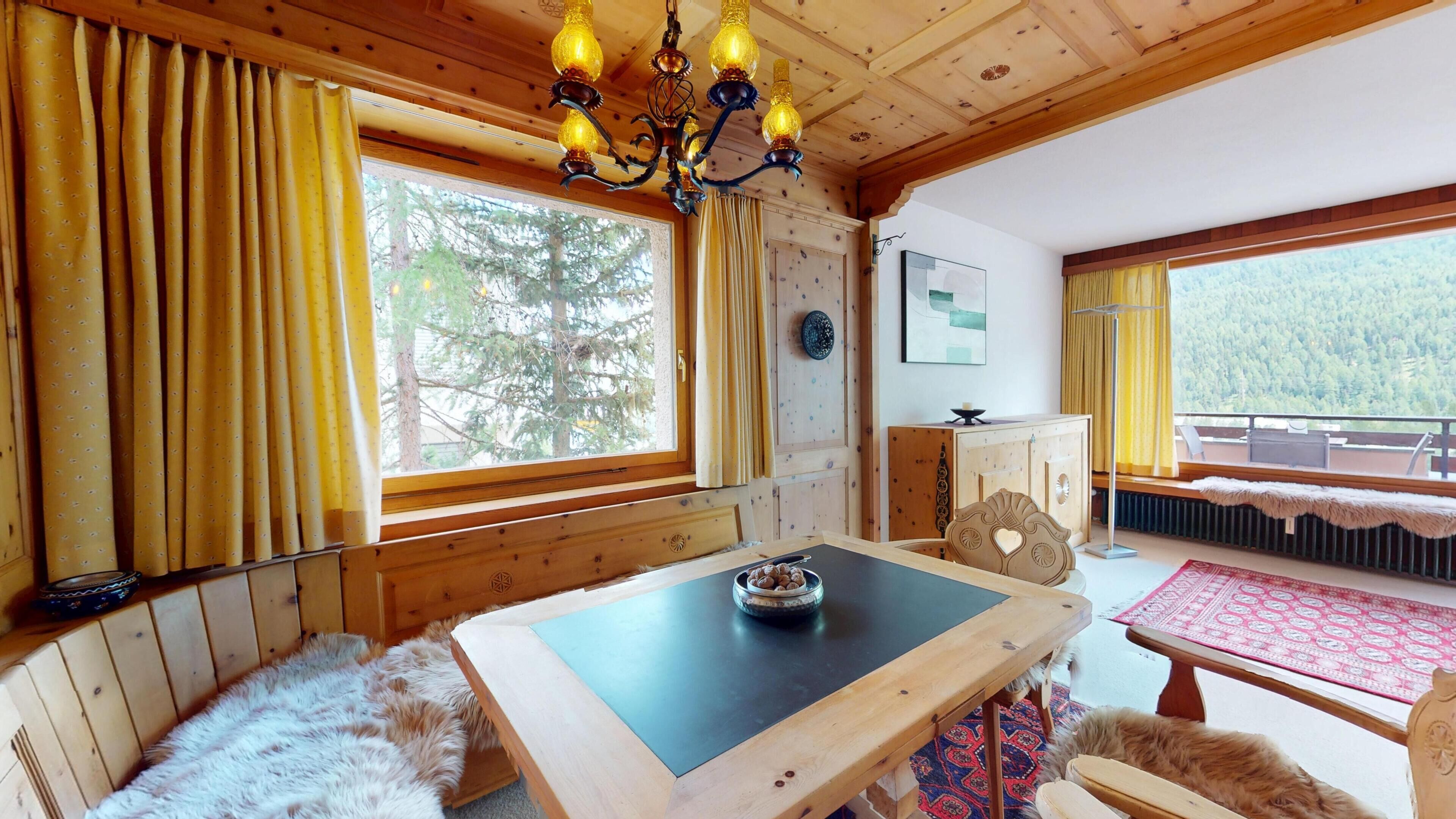 Ein gemütliches Blockhaus-Interieur mit Holztisch, fellbezogenem Sitz und einer Chandelieber.