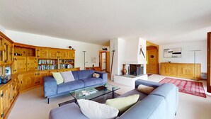 Un salon avec un canapé bleu, une table basse en verre, des étagères en bois et une cheminée.