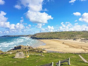 Paisagem costeira com praia, afloramentos rochosos e área gramada com cerca.