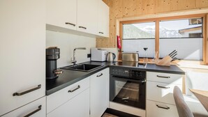 A modern kitchen with white cabinets, a black countertop, a coffee maker, a toaster, a kettle, and a stove. - Chalet With Mountain Scenery Your Bichelbach (Bichlbach)