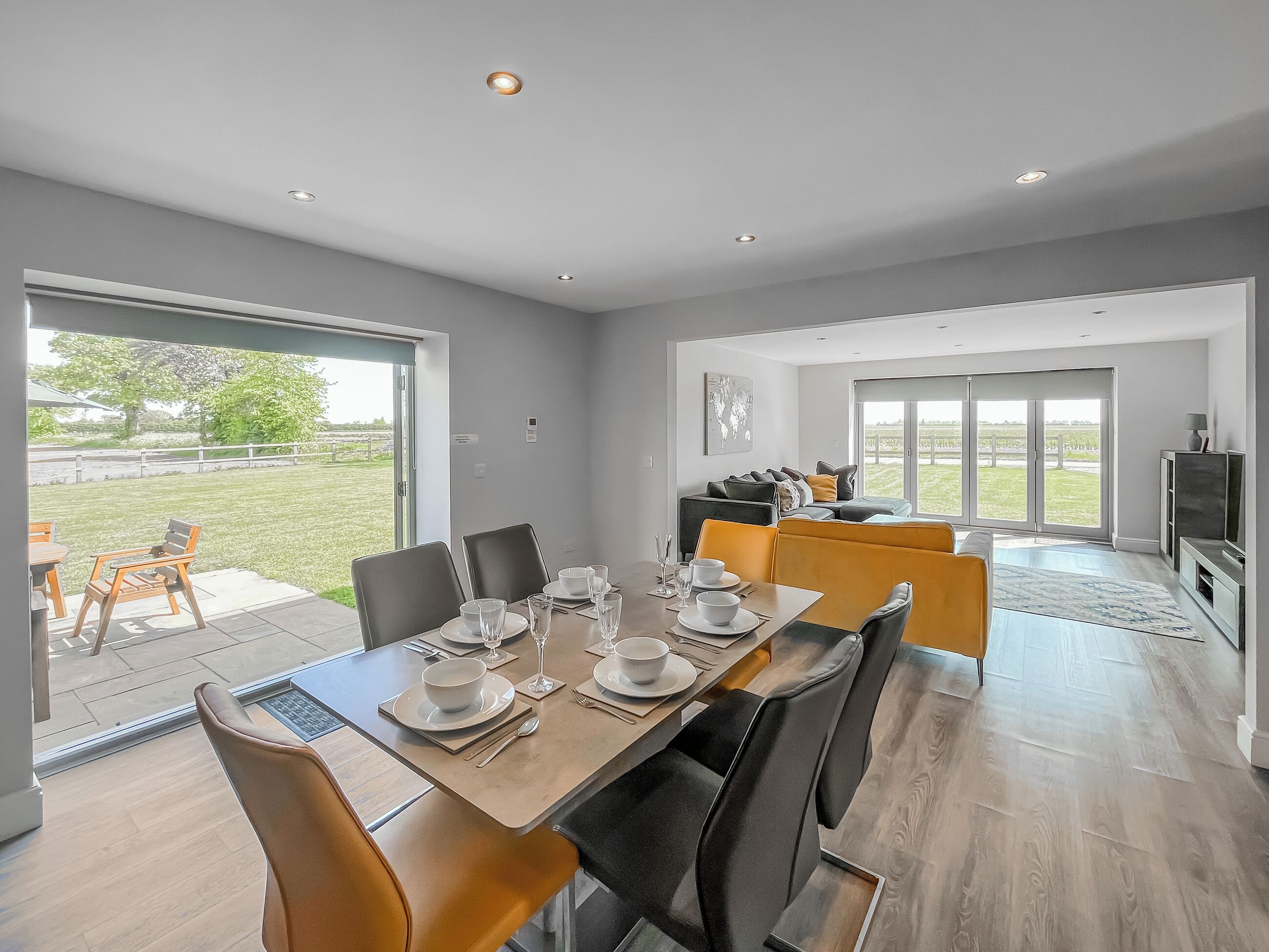 A modern dining area with a table set for four, a sofa in the background, and a view of the outdoors.