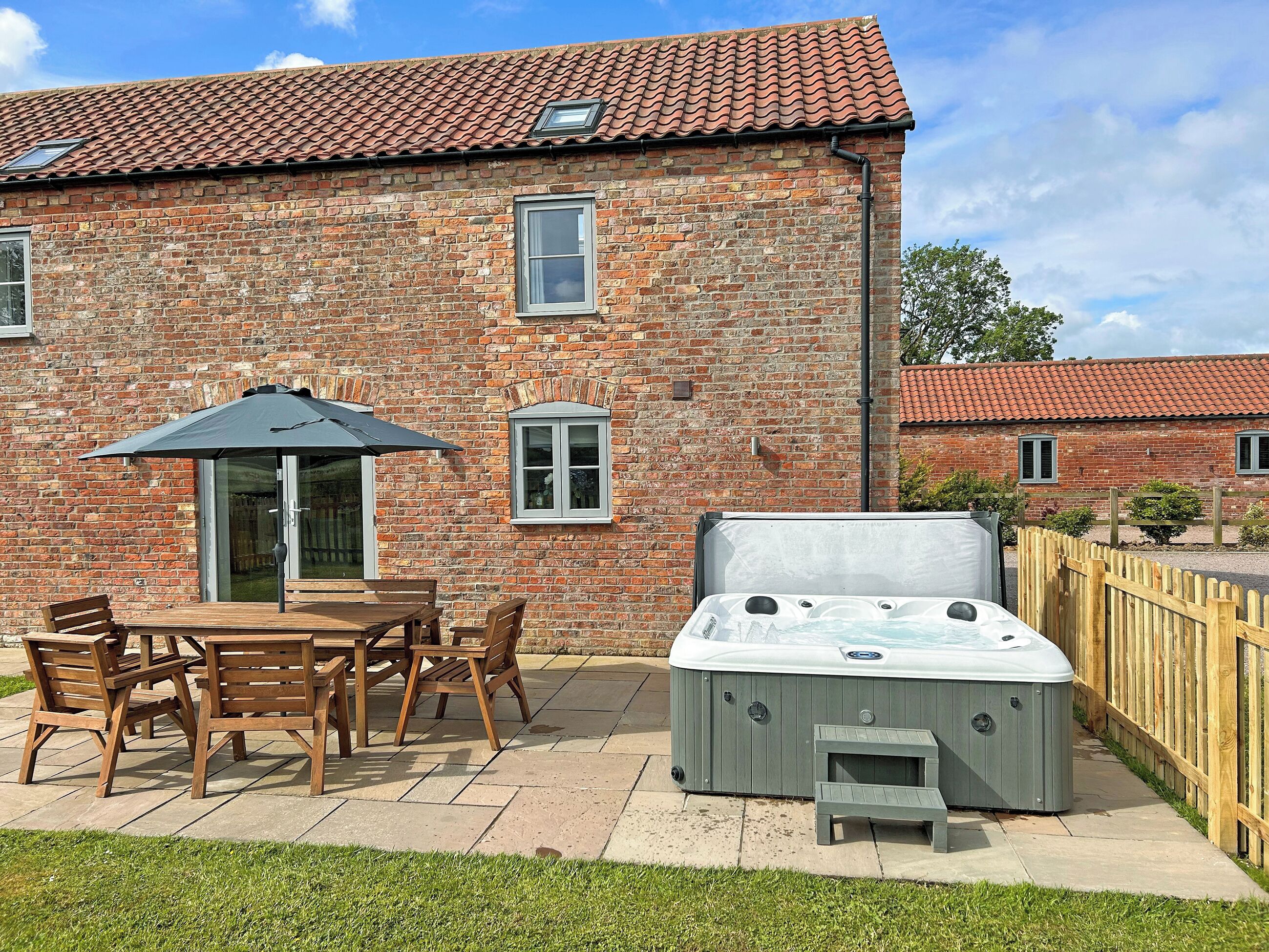 A brick house with a patio, a hot tub, and a wooden fence.