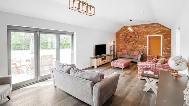 Un soggiorno moderno con un divano grigio, pavimento in legno, una parete decorata in mattoni e un'ampia finestra.