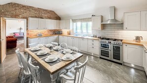 Una cucina moderna con mobili bianchi, una parete decorata con mattoni, un'area pranzo con tavolo in legno e sedie bianche, e un'ampia finestra che lascia entrare la luce naturale.