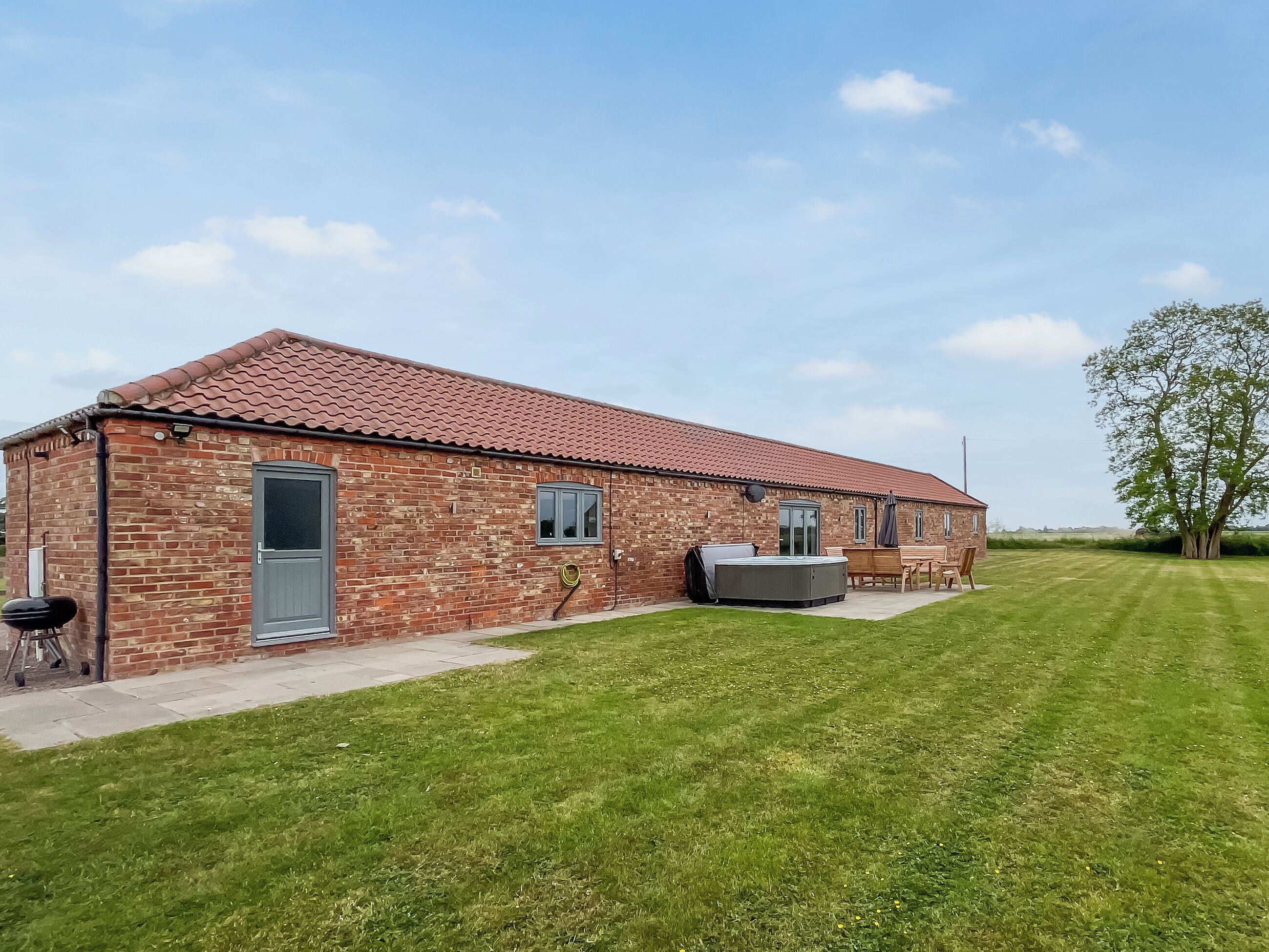 A brick building with a tiled roof, a door, windows, and a patio area with outdoor furniture.