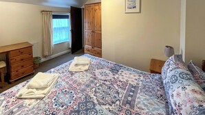 Ein Schlafzimmer mit einem Bett, einem Schminktisch, einem Kleiderschrank, einem Fenster mit Vorhängen und einem gerahmten Bild an der Wand.