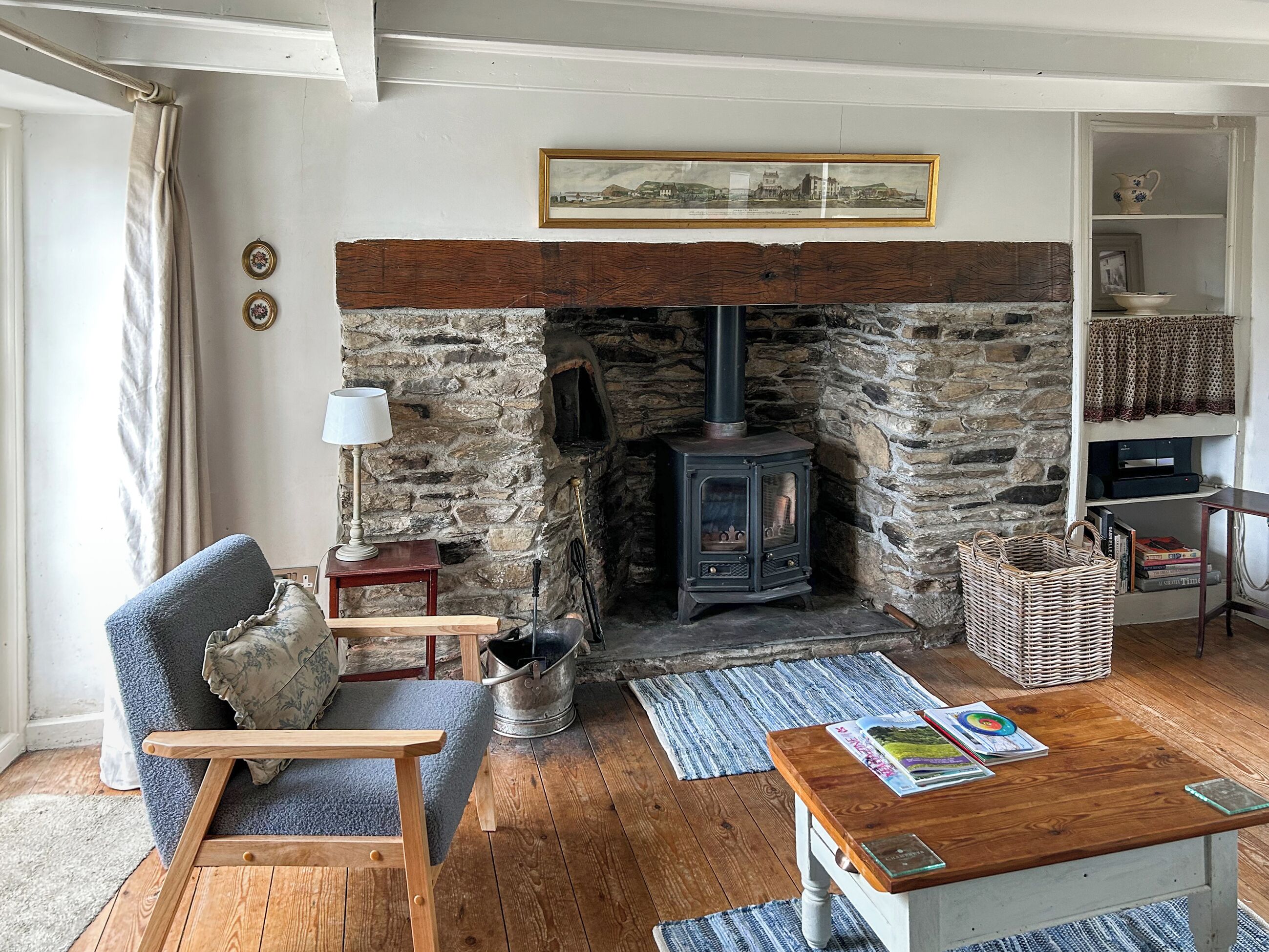 A cozy living room with a stone fireplace, a wooden table, a blue armchair, and a bookshelf.