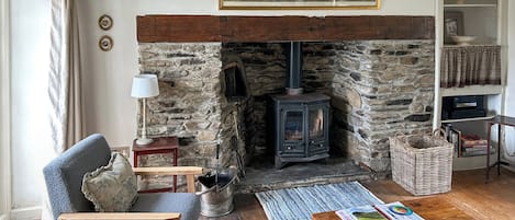 A cozy living room with a stone fireplace, a wooden table, a blue armchair, and a bookshelf.