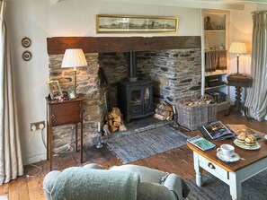 A cozy living room with a stone fireplace, a wooden table with a magazine and a cup, and a comfortable sofa. - 2 bedroom accommodation in Veryan (Veryan)