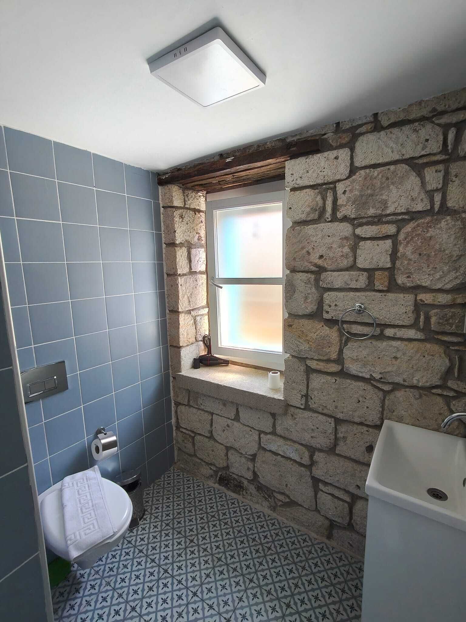 A bathroom with a toilet, sink, and a window with a stone wall.