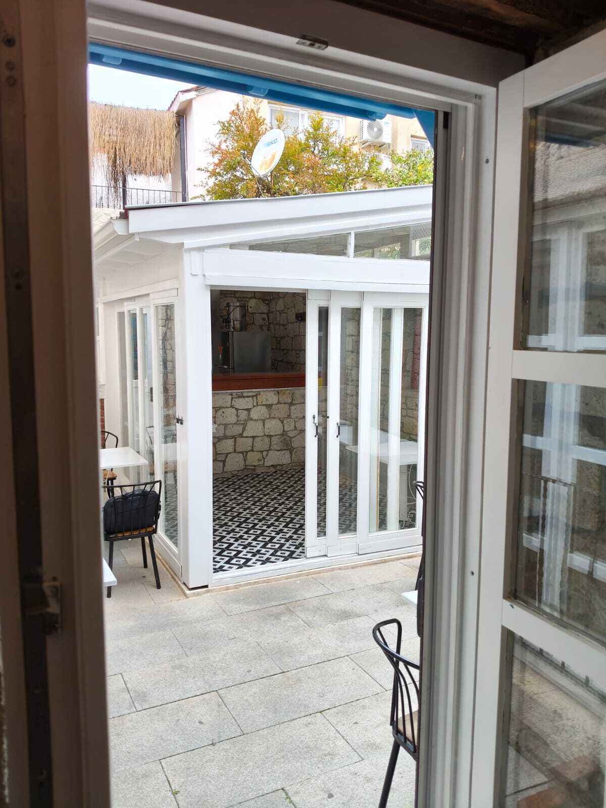 Vista a través de una puerta de cristal hacia un patio con pared de piedra, una mesa y una silla.