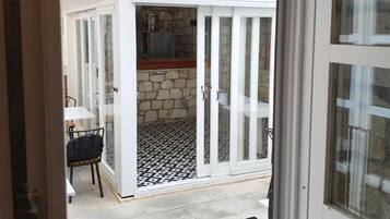 Vista a través de una puerta de cristal hacia un patio con pared de piedra, una mesa y una silla.