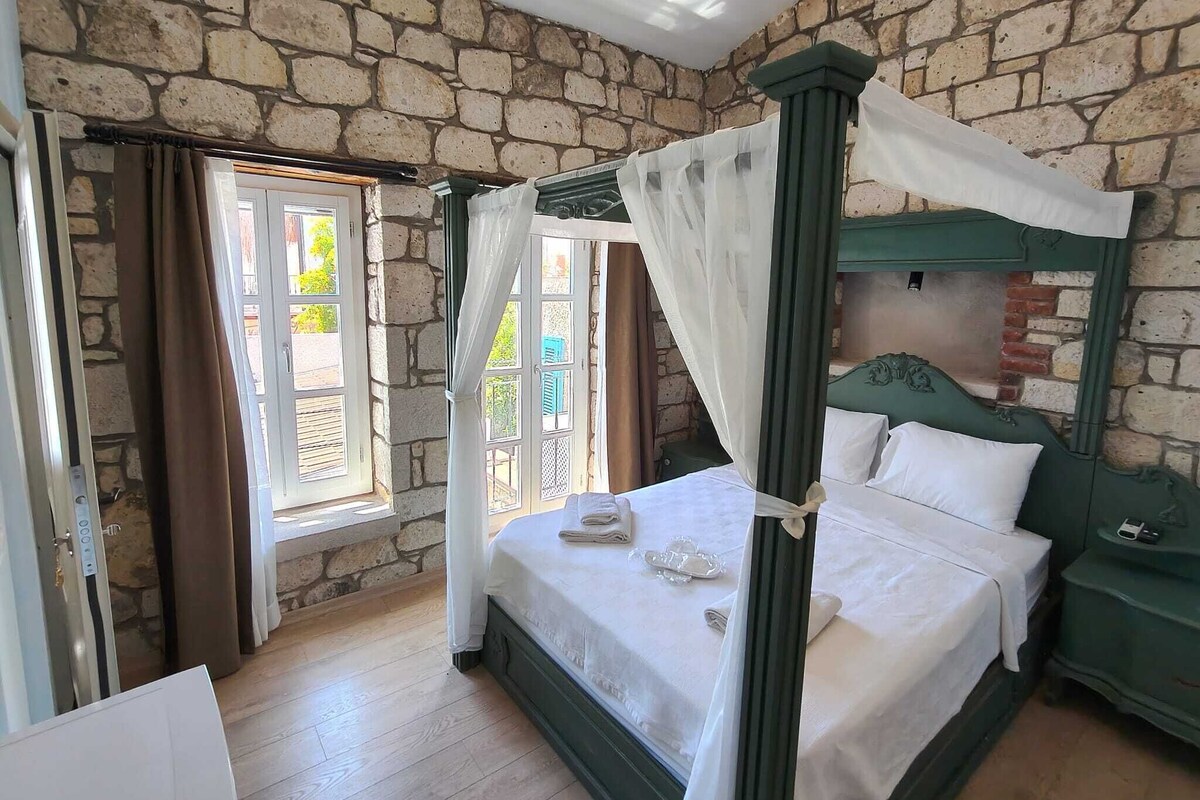 A room with a stone wall, a four-poster bed, and a window with curtains.