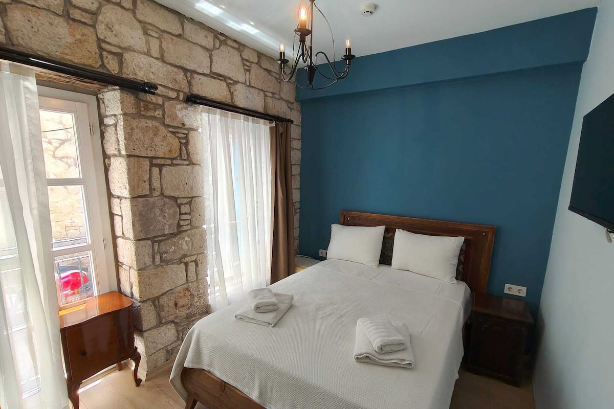Un dormitorio con pared de piedra, una cama de madera, una mesita de noche y una araña.