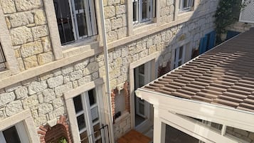 Un bâtiment en pierre doté de nombreuses fenêtres, un espace extérieur aménagé avec des tables et des chaises, et un sol à motifs.