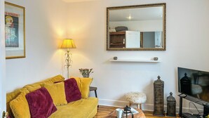 Un salón con sofá, mesa de centro, lámpara, televisor, altavoces y elementos decorativos.