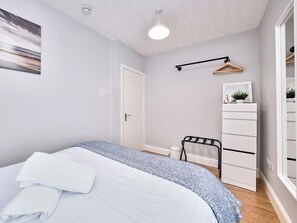 Ein Schlafzimmer mit einem Bett, einem Schminktisch, einer Kleiderstange und einer Deckenleuchte.