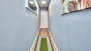 Passadís estret amb una porta blanca al final, un rug pla de disseny verd i blanc, i un ampli quadre floral a la paret.