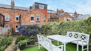 A residential garden with a white table and bench, brick houses, and a hedge. - 3 bedroom accommodation in Scarborough (Scarborough)
