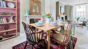A dining area with a wooden table set for four, surrounded by chairs. A bookshelf with books and decorative items is to the left. - 3 bedroom accommodation in Scarborough (Scarborough)