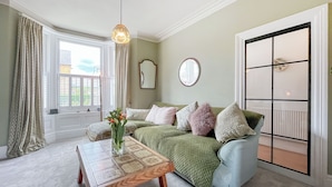 A room with a green sofa, a wooden coffee table, a hanging light fixture, a mirror, and a window with curtains. - 3 bedroom accommodation in Scarborough (Scarborough)