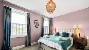 A bedroom with a bed, curtains, a mirror, a hanging light fixture, and a nightstand. - 3 bedroom accommodation in Scarborough (Scarborough)