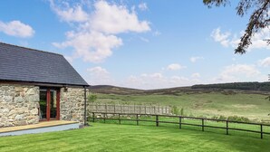 A stone building with a dark roof, a wooden deck, and a view of a grassy field and hills. - 1 bedroom accommodation in Rogart (Rogart)