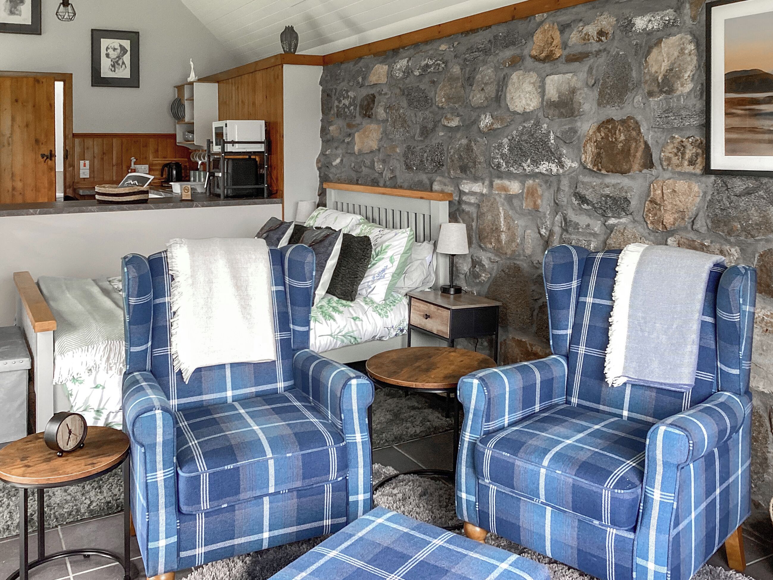 A cozy room with a stone wall, a bed with a headboard, a coffee machine, and a small table with a lamp.