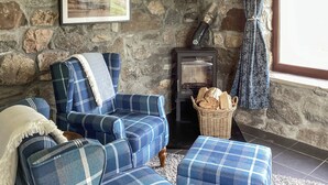 A stone-walled room with a blue plaid sofa, a small wooden table, and a fireplace. - 1 bedroom accommodation in Rogart (Rogart)