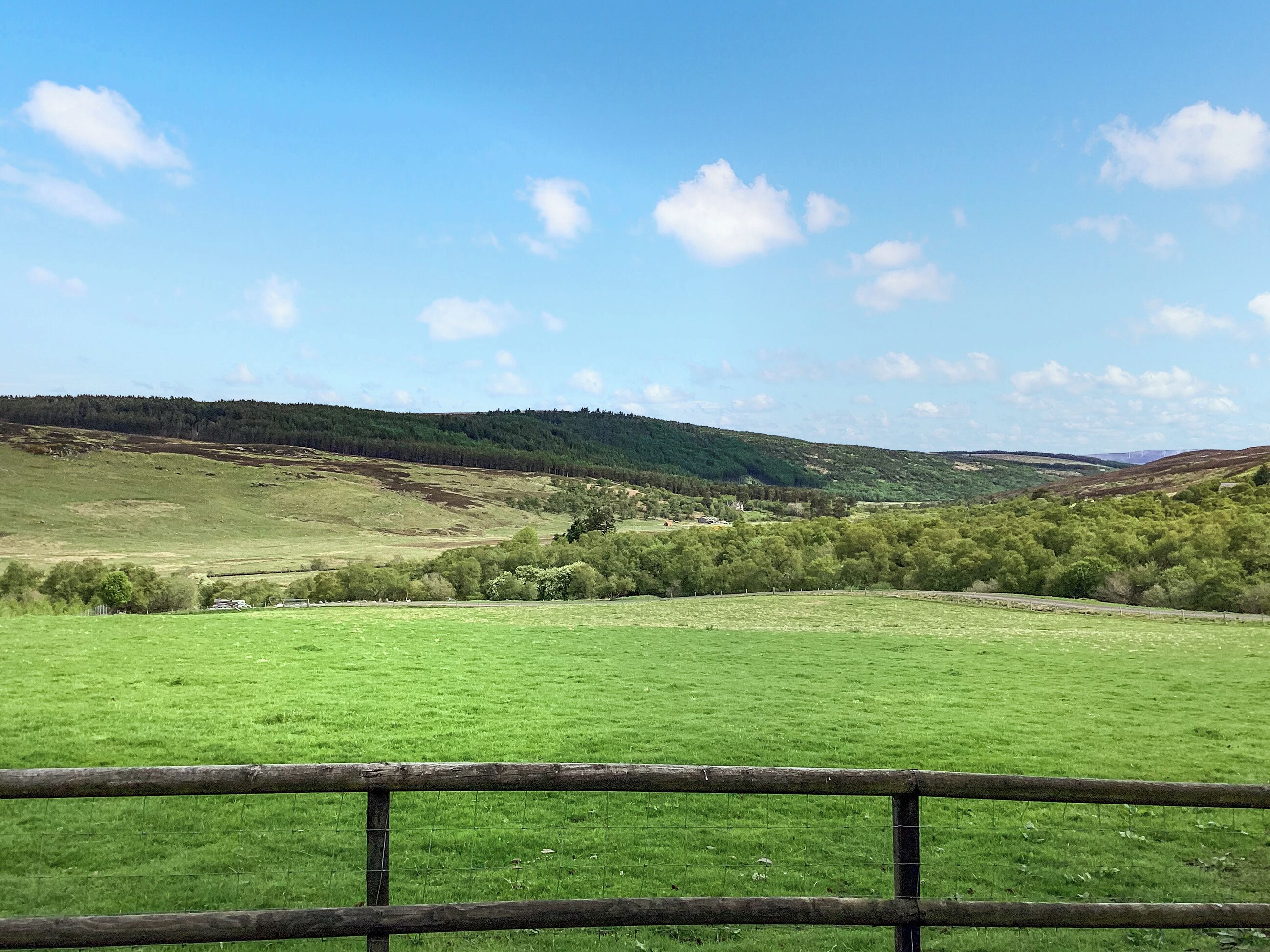 A rural landscape with rolling hills, a fenced field, and a clear sky.
