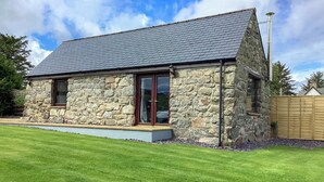 A stone building with a sloped roof, large windows, and a well-maintained lawn. - 1 bedroom accommodation in Rogart (Rogart)