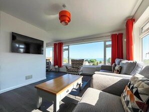 A modern living room with a sofa, a wooden coffee table, and a television mounted on the wall. - 3 bedroom accommodation in Paignton (Paignton)