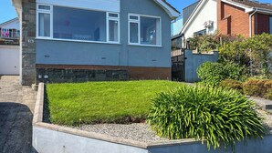 Uma casa de dois andares com um jardim frontal, uma garagem visível e uma chaminé de tijolos.