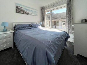 Ein Schlafzimmer mit einem Bett, einem Nachttisch, einer Kommode, einem Fenster mit Vorhängen und einem Bild an der Wand.