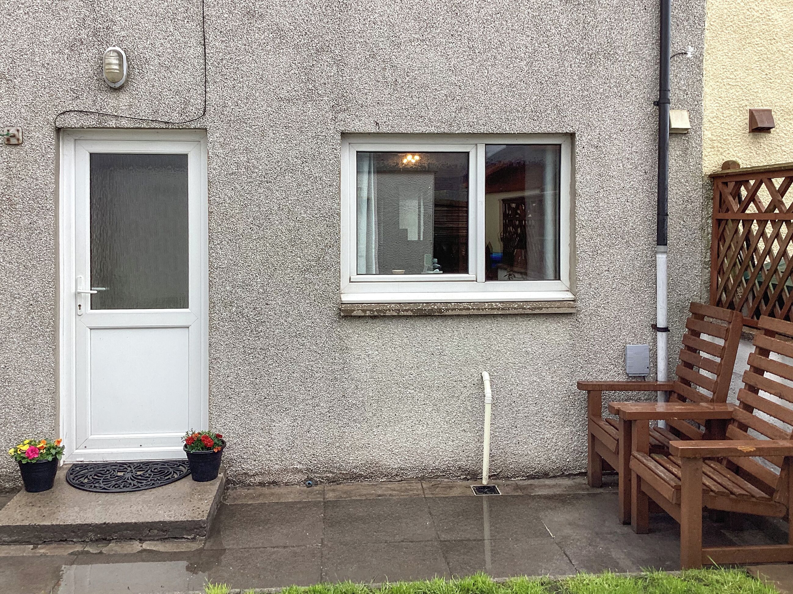 A residential building with a white door, a window, a bench, and potted plants.