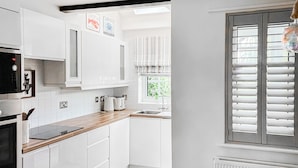 Een moderne keuken met witte kasten, een houten aanrecht, een ingebouwde oven en een raam met zonwering.