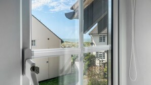 Een raam met uitzicht op een huis, een deurklink en een witte parelsnoer aan de muur.