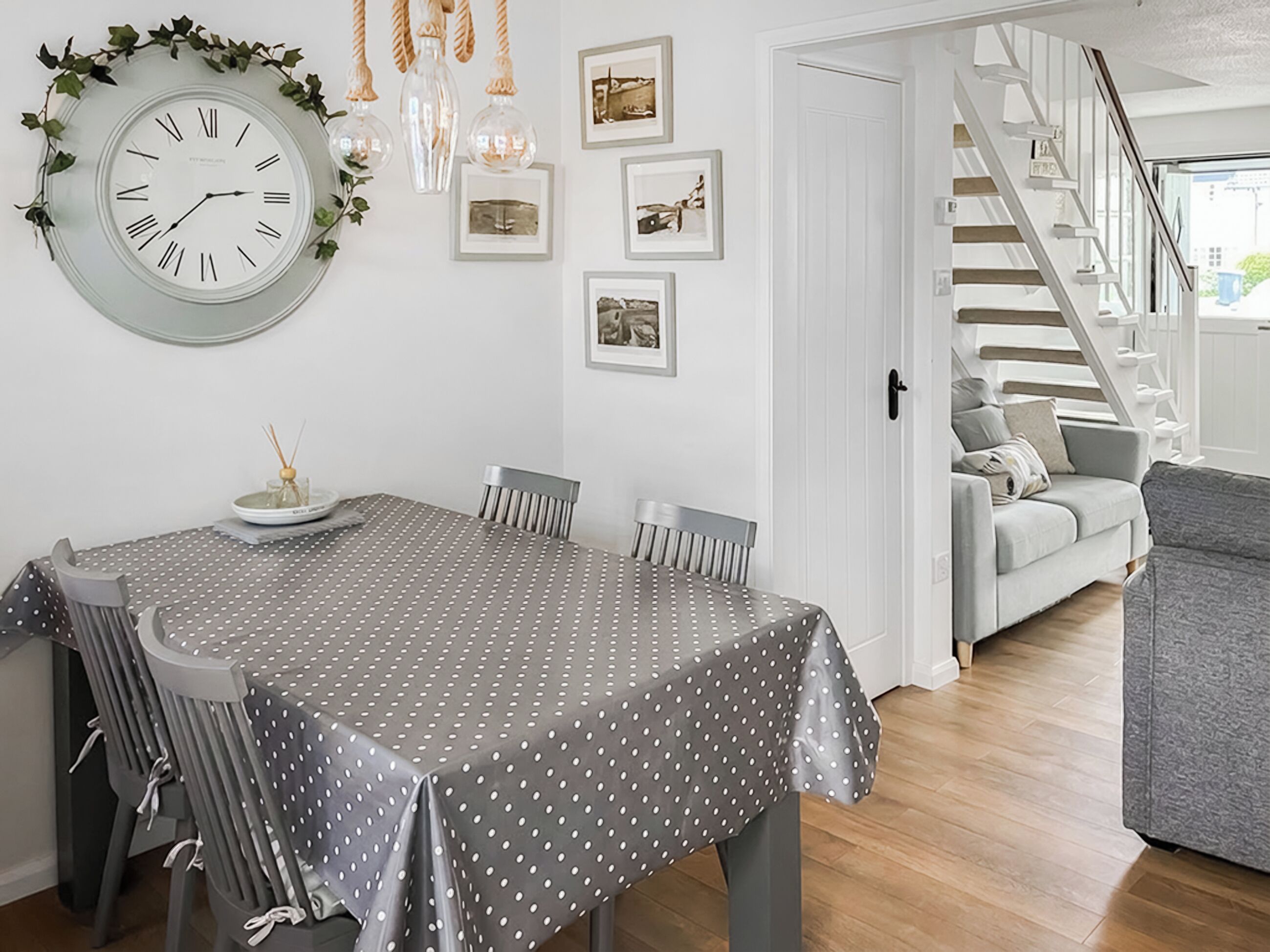 A dining area with a round wall clock, a polka dot tablecloth, and a staircase leading to a living area.