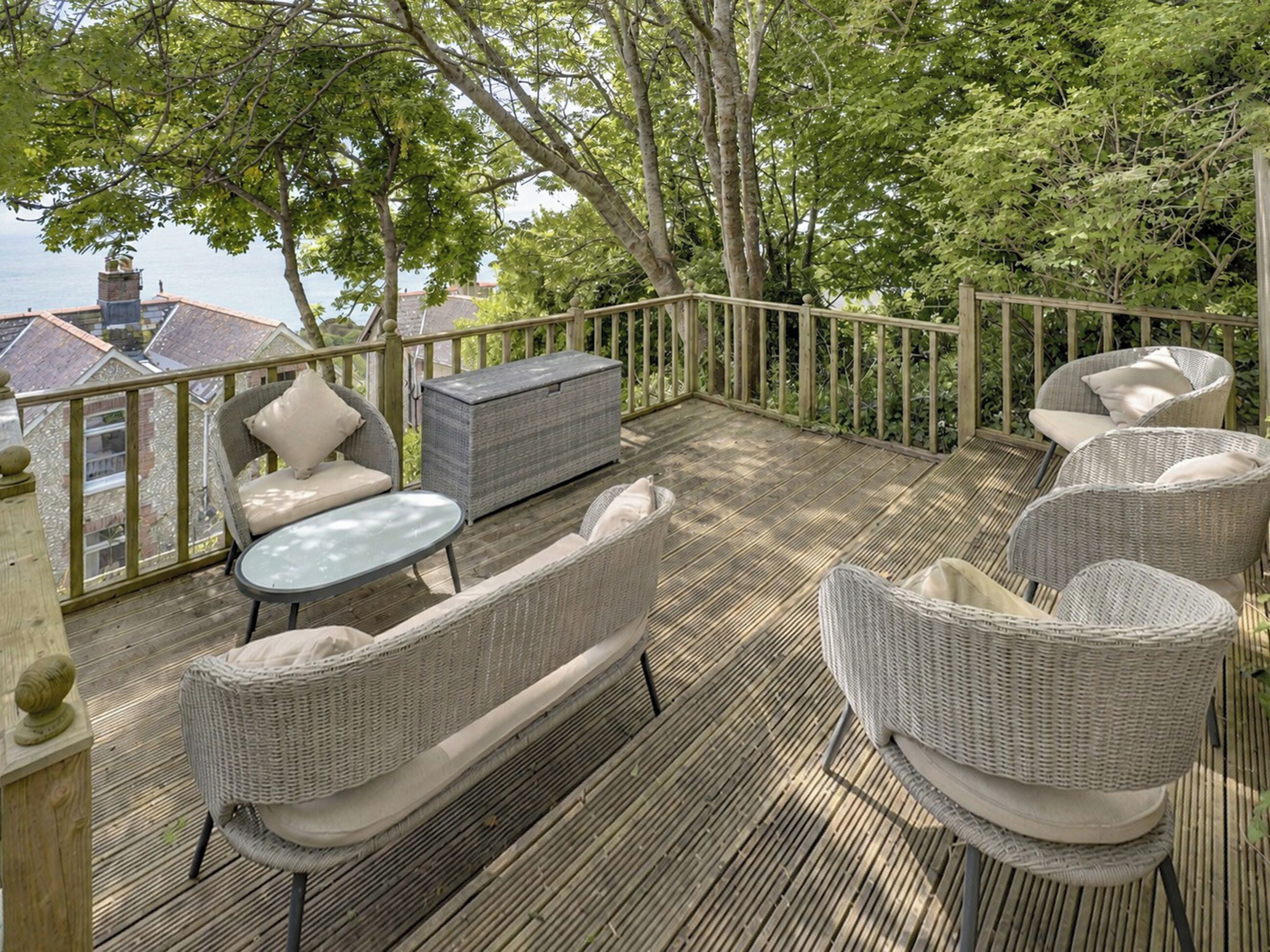 Une terrasse dotée de meubles en osier, d’une table ronde et d’un coffre de rangement.