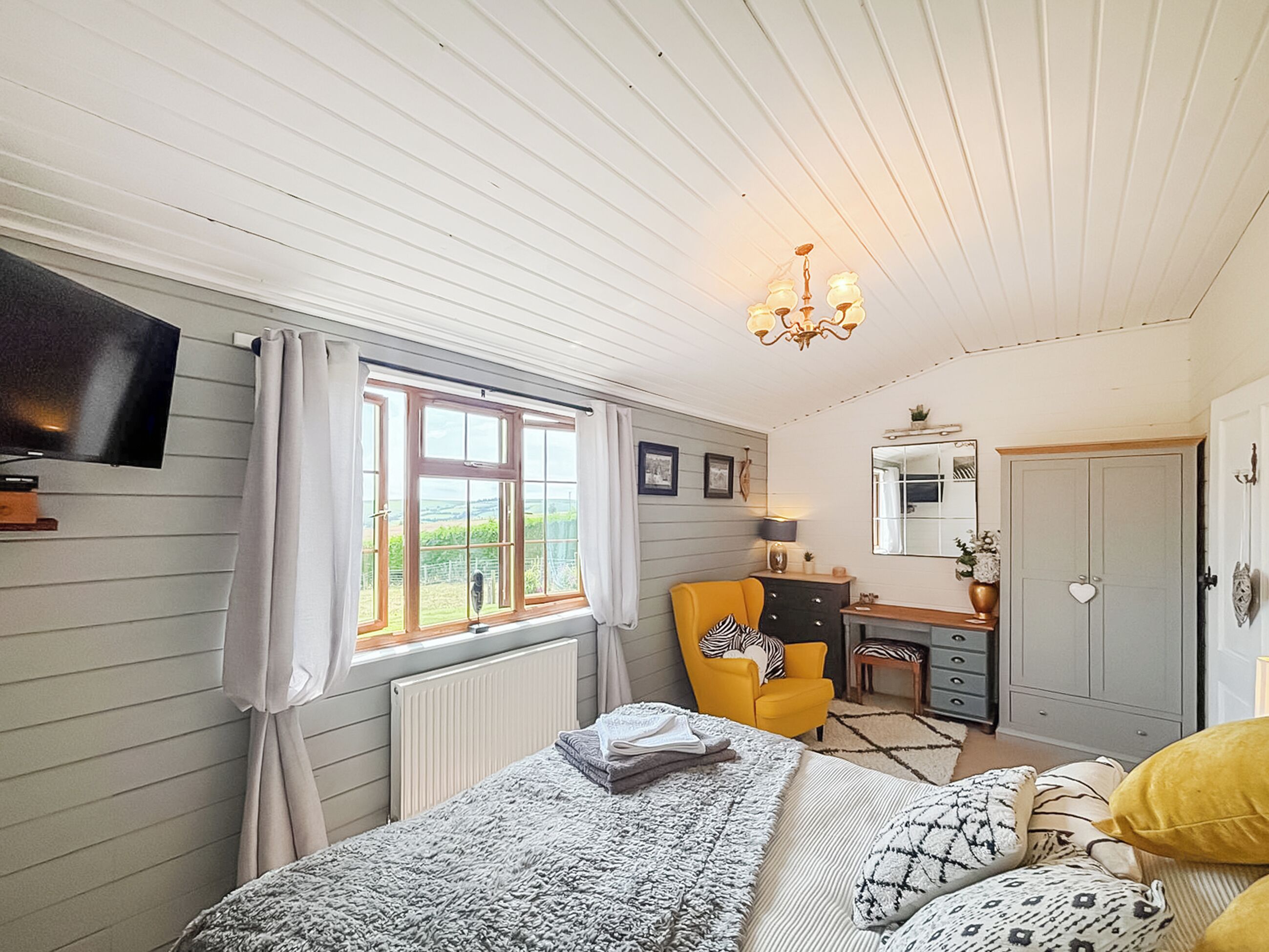 Un dormitorio con cama, escritorio, silla, televisor y ventana con cortinas.