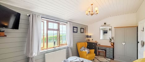 A bedroom with a bed, a desk, a chair, a television, and a window with curtains.
