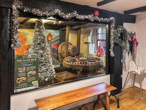 A room with a wooden bench, a large window displaying a Christmas tree and a mechanical device, and a wall-mounted clock. - 4 bedroom accommodation in Skipton (Skipton)