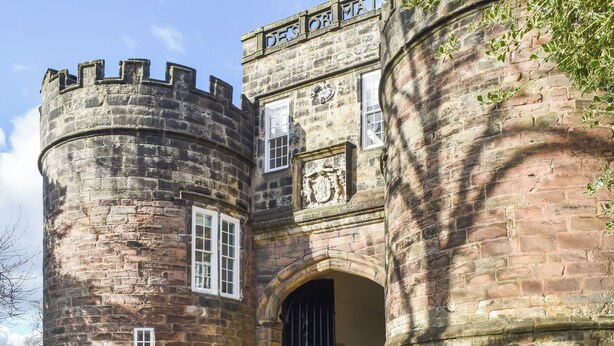 Ein historisches Steinhaus mit einem runden Turm, einem Rundbogenportal und einem Wappen.