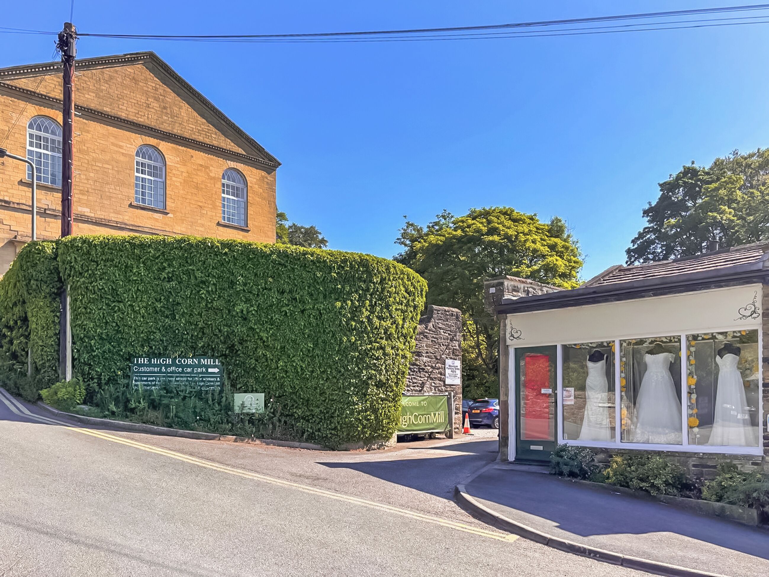 A brick building with a sign for 'The High Corn Mill' and a shop with wedding dresses.