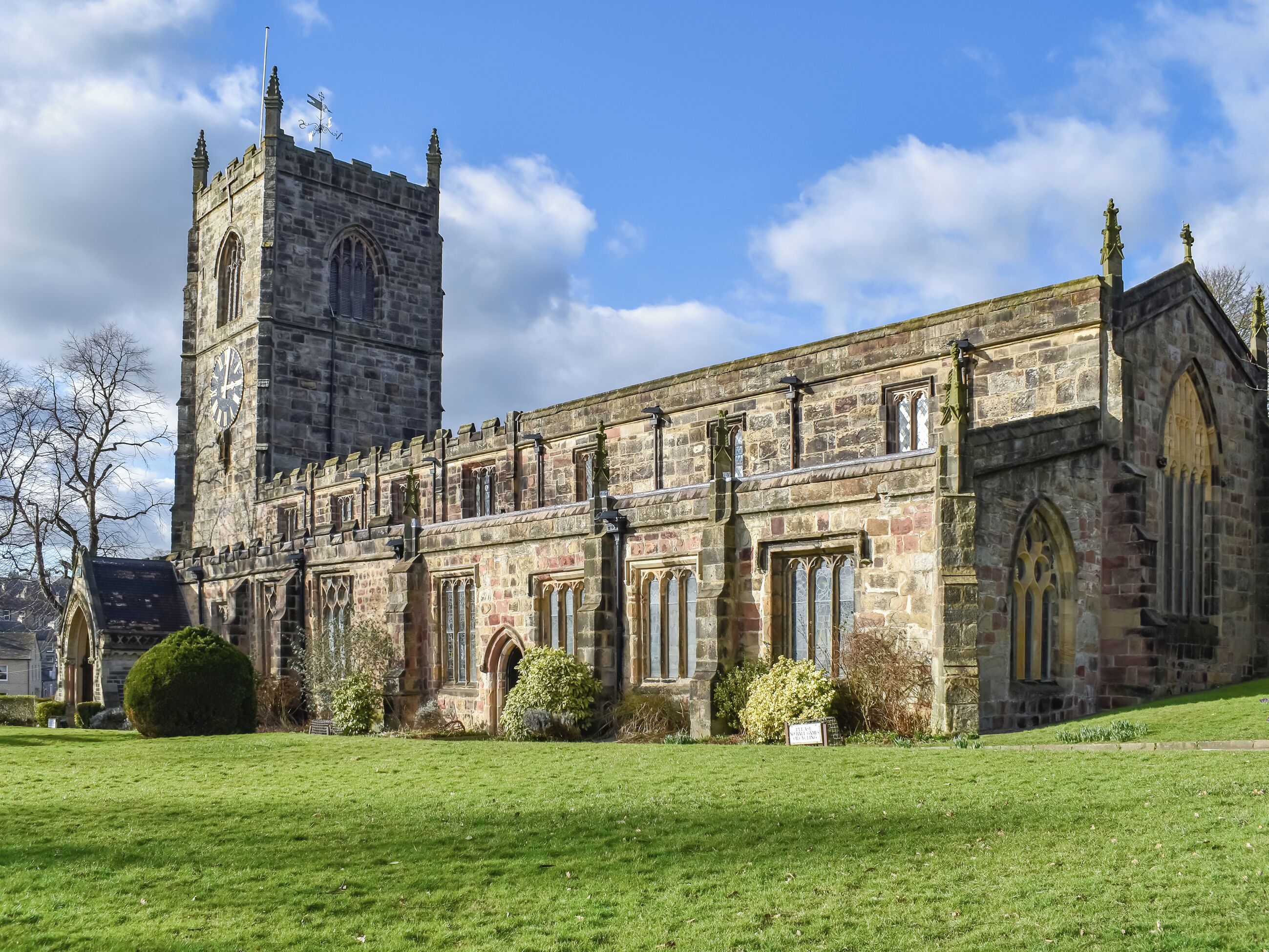 A historic stone building with a prominent clock tower, arched windows, and a well-maintained lawn.