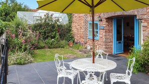 A patio with a round table and chairs, a yellow umbrella, and a stone building with blue doors. - 3 bedroom accommodation in Cheddar (Cheddar)