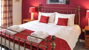 A hotel room with a bed, two bedside tables, a red wall, and a window with curtains. - 3 bedroom accommodation in Cheddar (Cheddar)